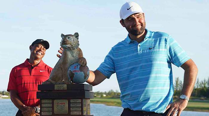 Scottie Scheffler, right, poses with the trophy as Tiger Woods smiles in the background, after winning the Hero World Challengeat the Albany Golf Club, in New Providence, Bahamas, Sunday, Dec. 3, 2023.